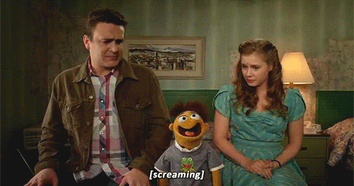 A muppet sitting between two humans screaming as they watch him.