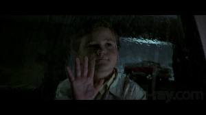 Timmy is a small boy with a cow lick hair style and he is looking out a rain filled window and pressing his hand against the glass with a creepy half smile on his face